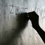 A silhouette hand writes on a chalkboard.