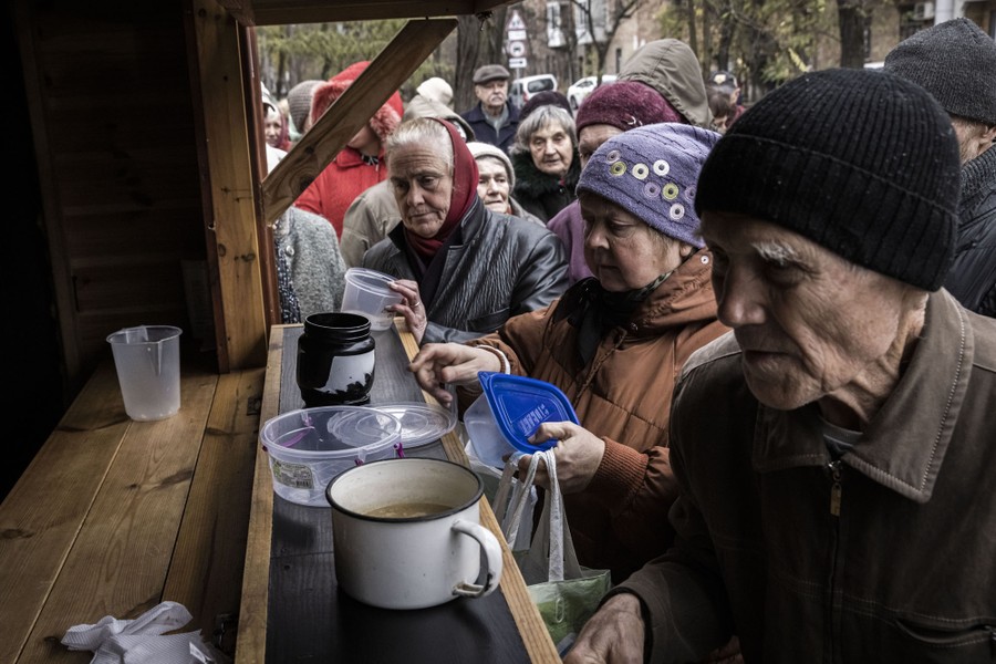 Older people line up at outside a stand, waiting for soup and hot food.