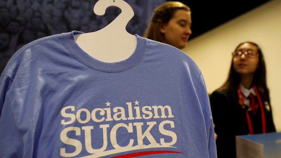 A T-shirt on a hanger reads "Socialism Sucks"; two young women stand behind it.