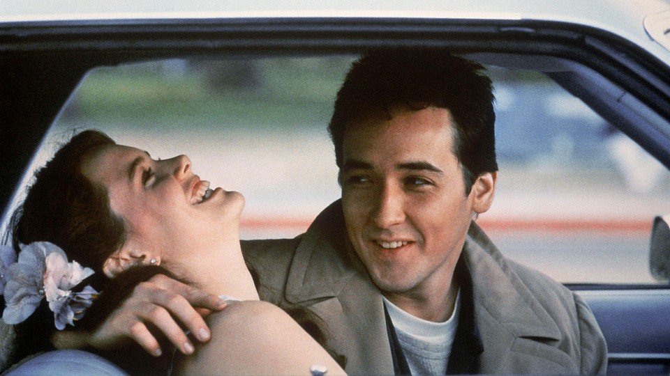 John Cusack and Ione Skye laugh together in a car.