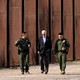 Biden walking with two police officers, the border wall in the background.