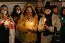 People stand with coats on holding lit candles