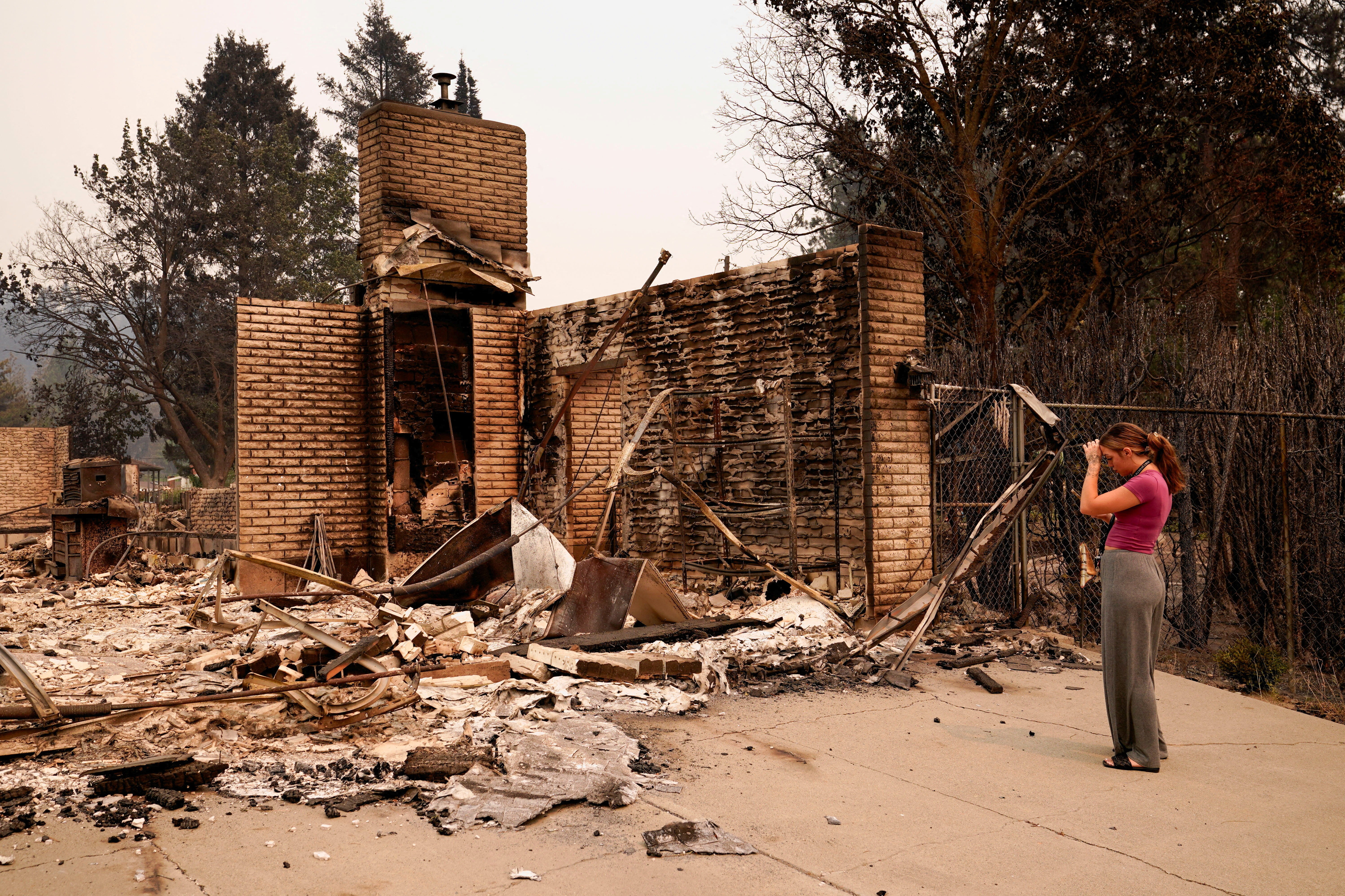 A woman stands in front of the rubble of a burned house.