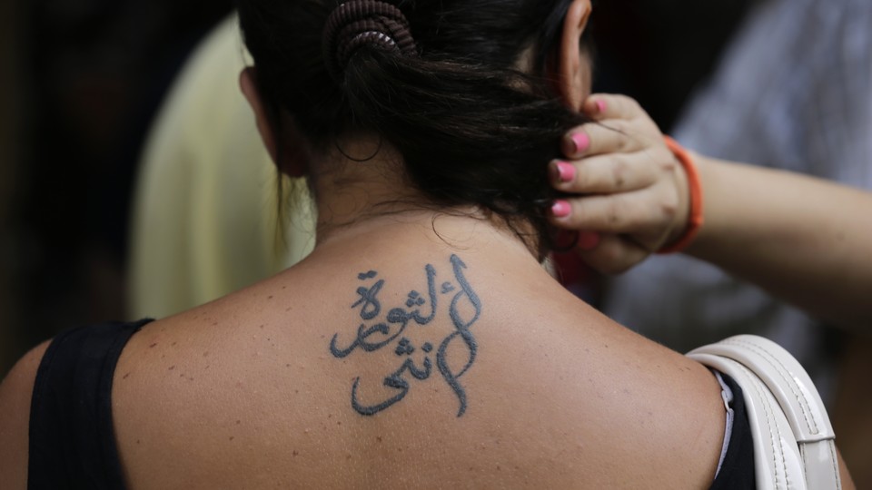 A person holds their hair up to reveal a tattoo in Arabic on their upper back.