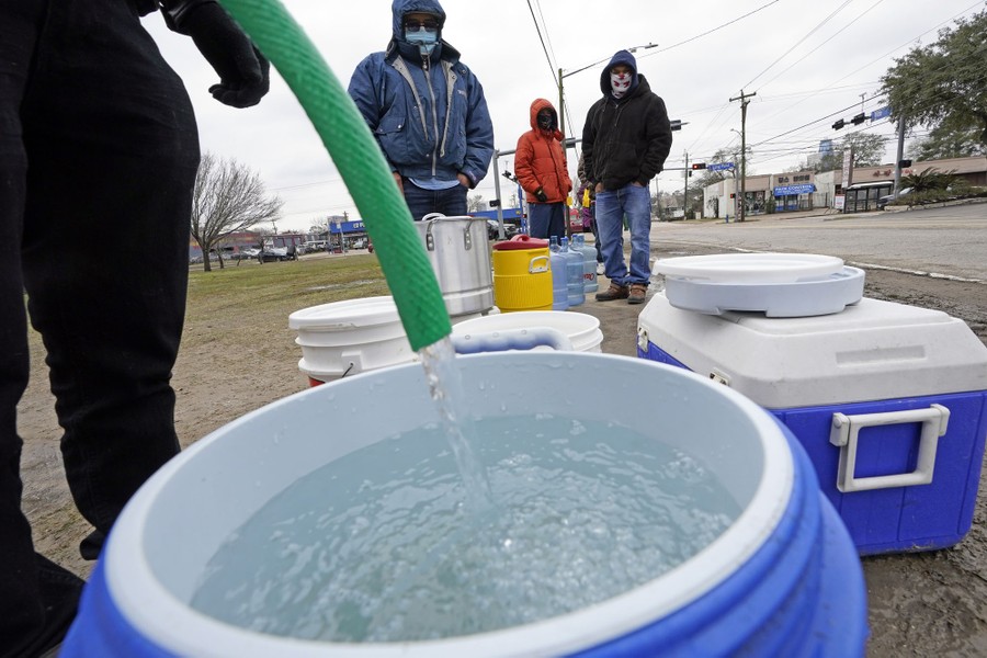 People stand at the edge of a park, with buckets and ice chests, waiting to fill them with fresh water.
