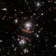 A view of many galaxies in deep space, with several of them smeared, distorted, and magnified in the center