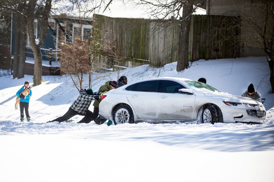 About five people push a car stuck in the snow.