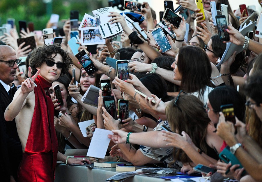 A large crowd reaches to take photos and get autographs as an actor stands nearby at a barrier.