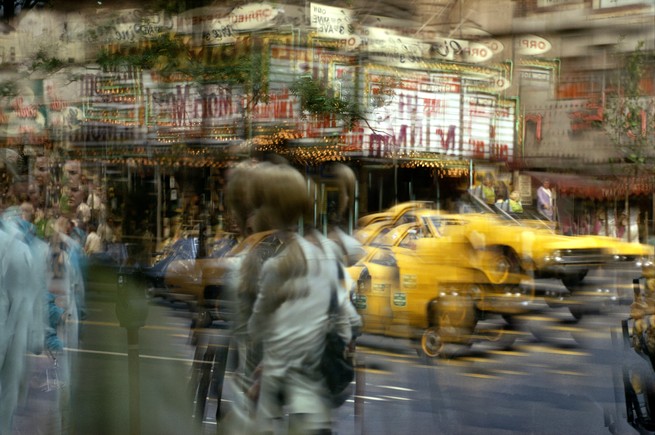A blurred image of a busy city intersection, with people and taxis in motion