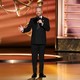 Nate Bargatze stands on the Emmys stage with a microphone