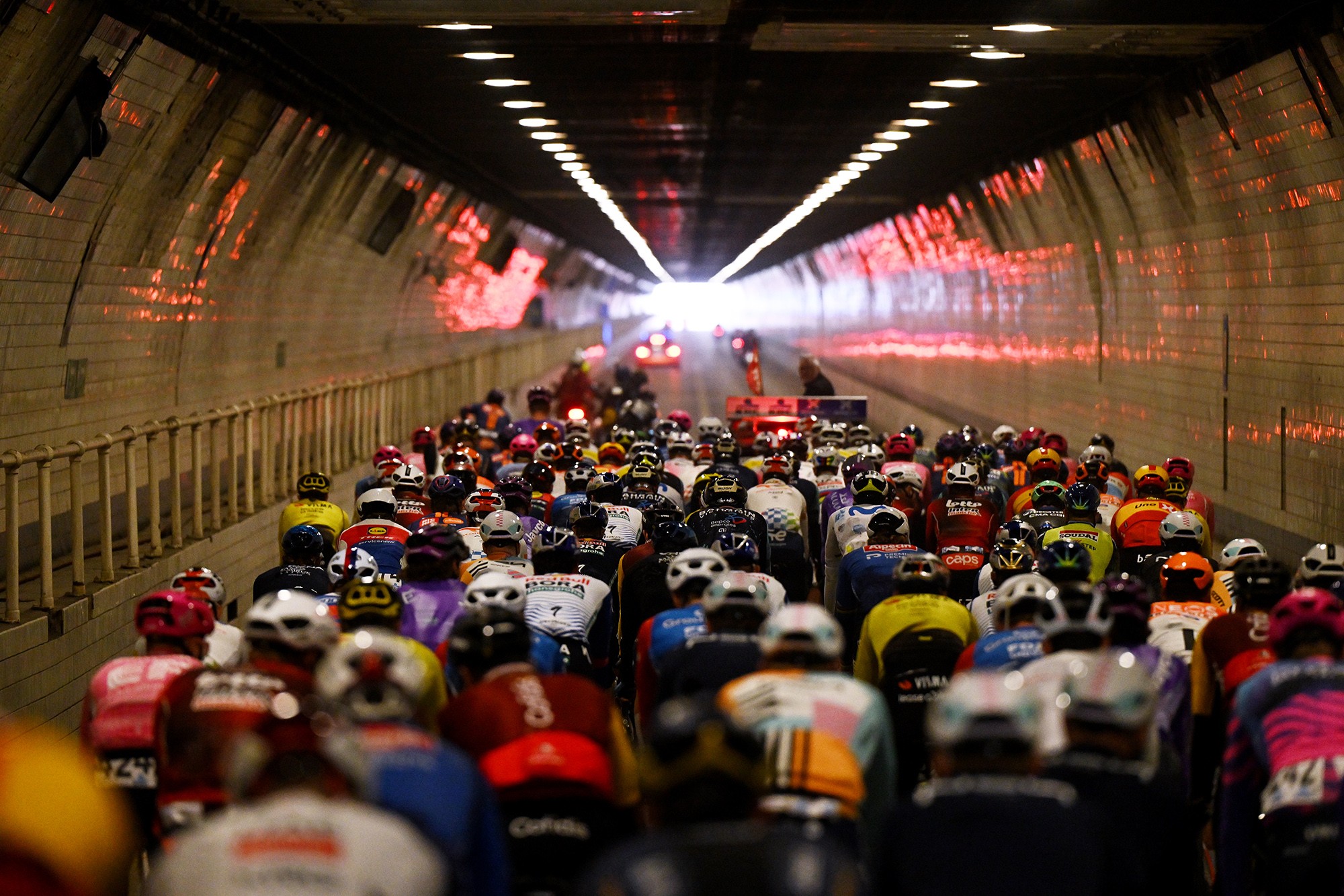 A view from behind of a pack of bicycle racers riding through a road tunnel.