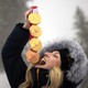 An athlete in a warm coat stands outside for a photo shoot, holding four Paralympic medals above their upturned face, pretending as if they might swallow them.
