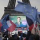 A crowd waves flags before a poster of French President Emmanuel Macron on the Eiffel Tower.