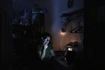 A woman reads from a mobile device in a dark room.