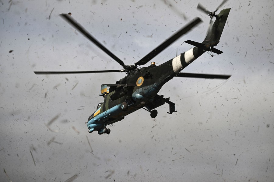 A military helicopter takes off, kicking up dust and debris.