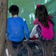 A boy and a girl sit on a barrel with their backs to the camera