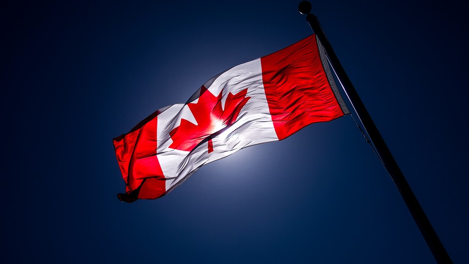 A Canadian flag, slightly darkened by the light, waves in the air.