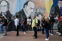 A loose queue of people in front of a wall featuring a mural of three men