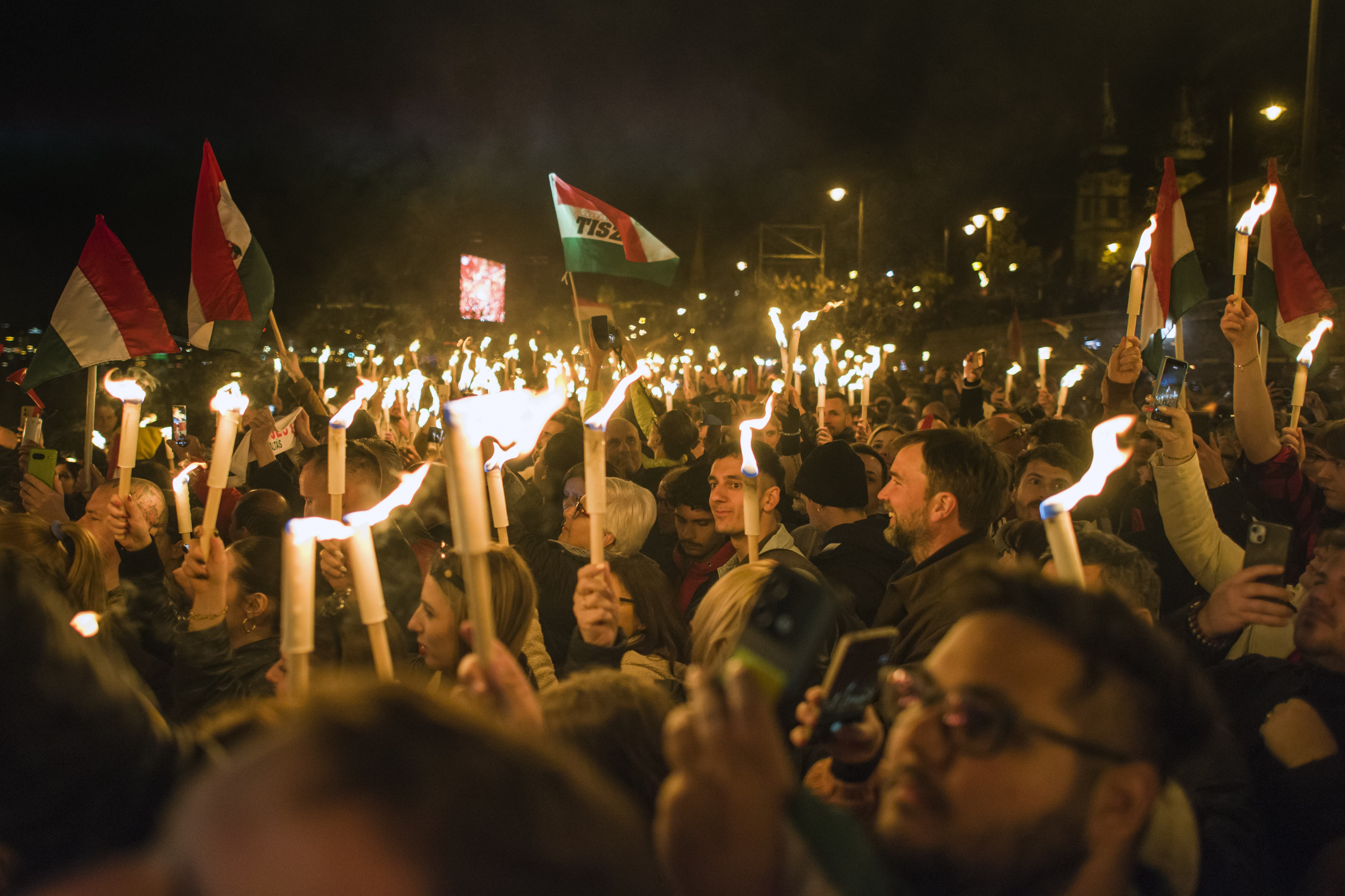 A crowd of people hold up glowing torches and light tubes during a rally.