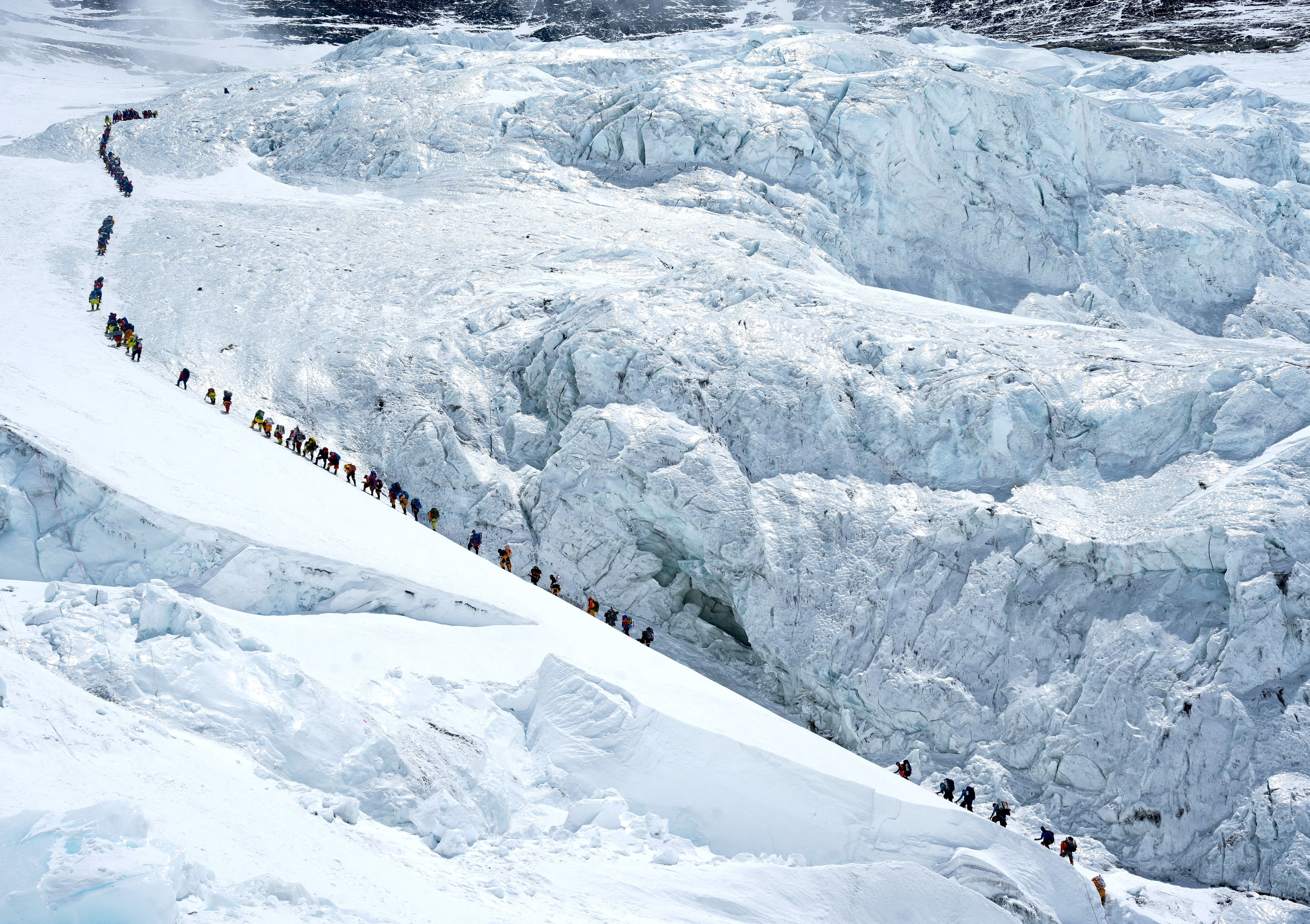 A long line of climbers walk up a steep slope along a glacier on Mount Everest.
