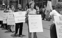 People demonstrate outside a building, with placards that read "No Restrictions on Our Rights" and "Abortion: A Woman's Right to Choose."