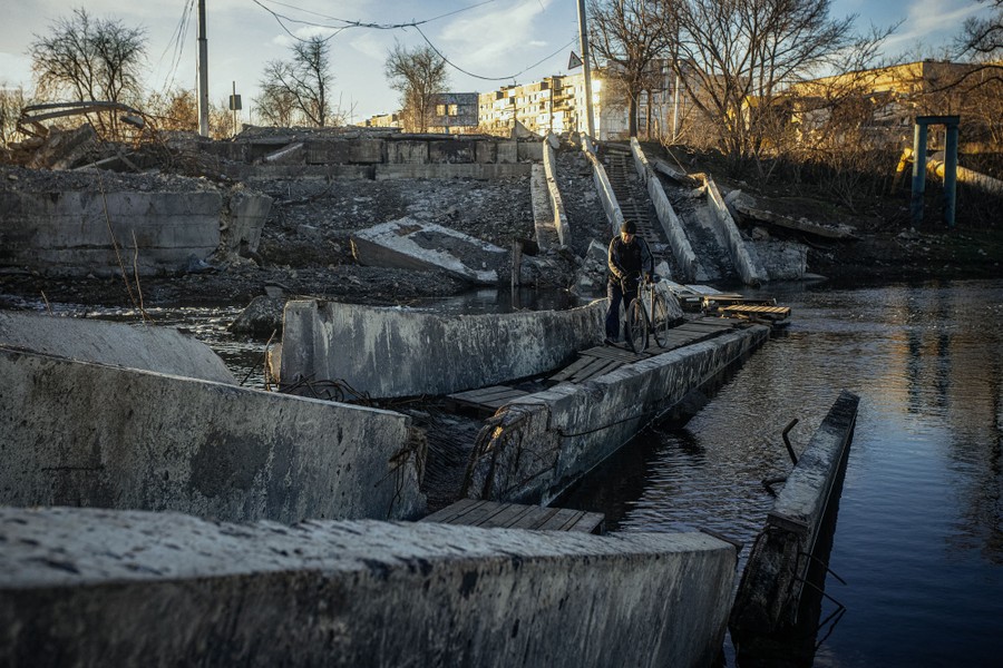A person walks their bicycle across a destroyed bridge in Ukraine.