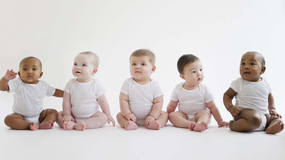 Five racially diverse babies sitting in a line wearing white onesies