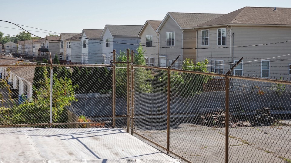 Barbed wire fencing, an empty lot, and a row of houses in a neighborhood on the South Side of Chicago.