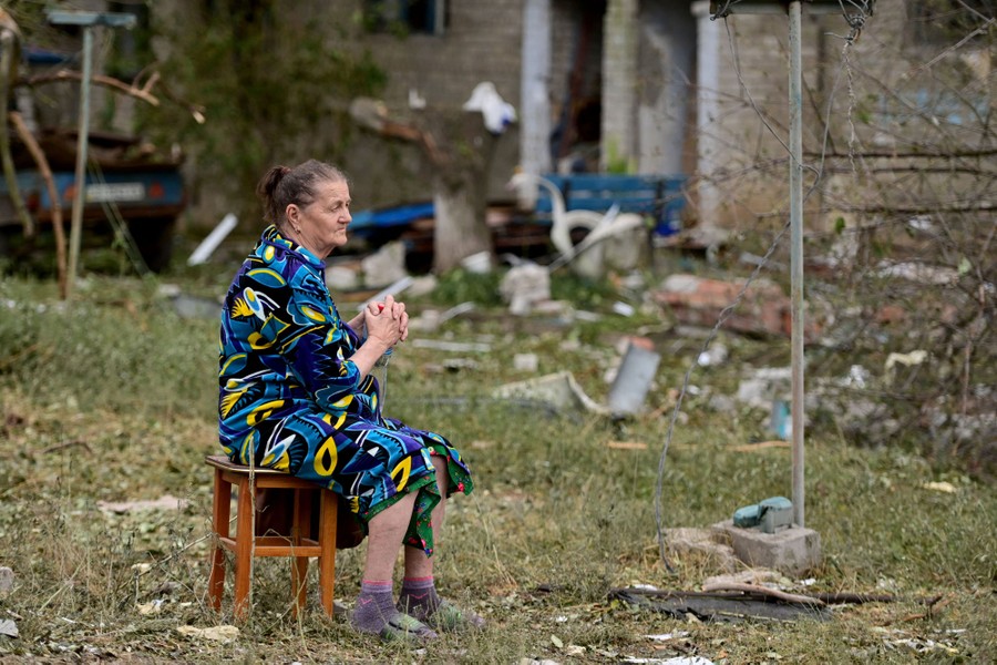 A woman sits in a wooden chair amid rubble from a missile strike.