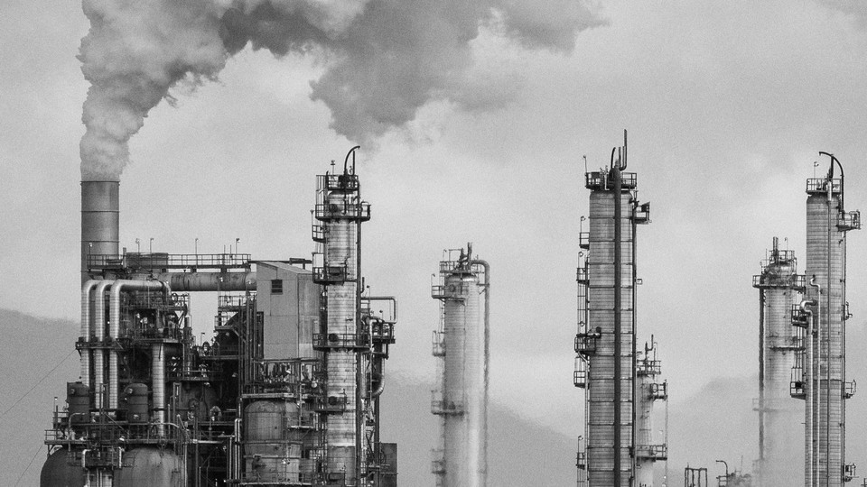 Smoke stacks at an oil refinery are shown against a gray sky