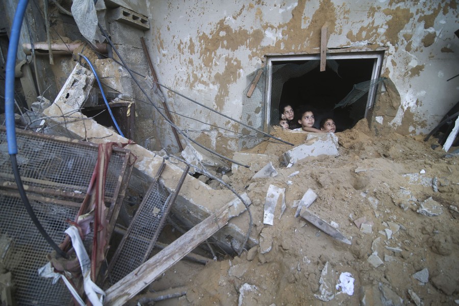 Several children peer through a broken window, overlooking piles of rubble after an air strike.