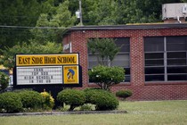 A sign reading "East Side High School: Top 500 High Schools in the U.S." sits outside a brick school building.