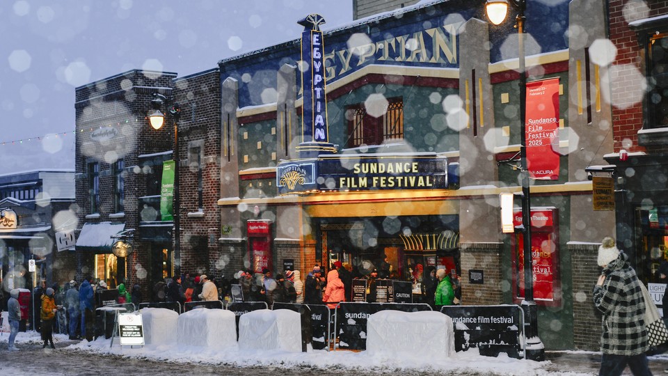 A color photograph showing people lined up outside the Egyptian Theatre on a snowy day at the Sundance Film Festival 2026 in Park City, Utah.