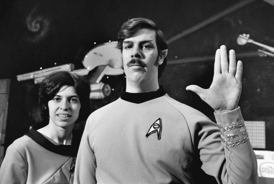 A man and woman, wearing Star Trek costumes, pose inside their memorabilia store.