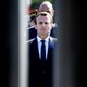 Emmanuel Macron stands framed between two doors with people lined up behind him.