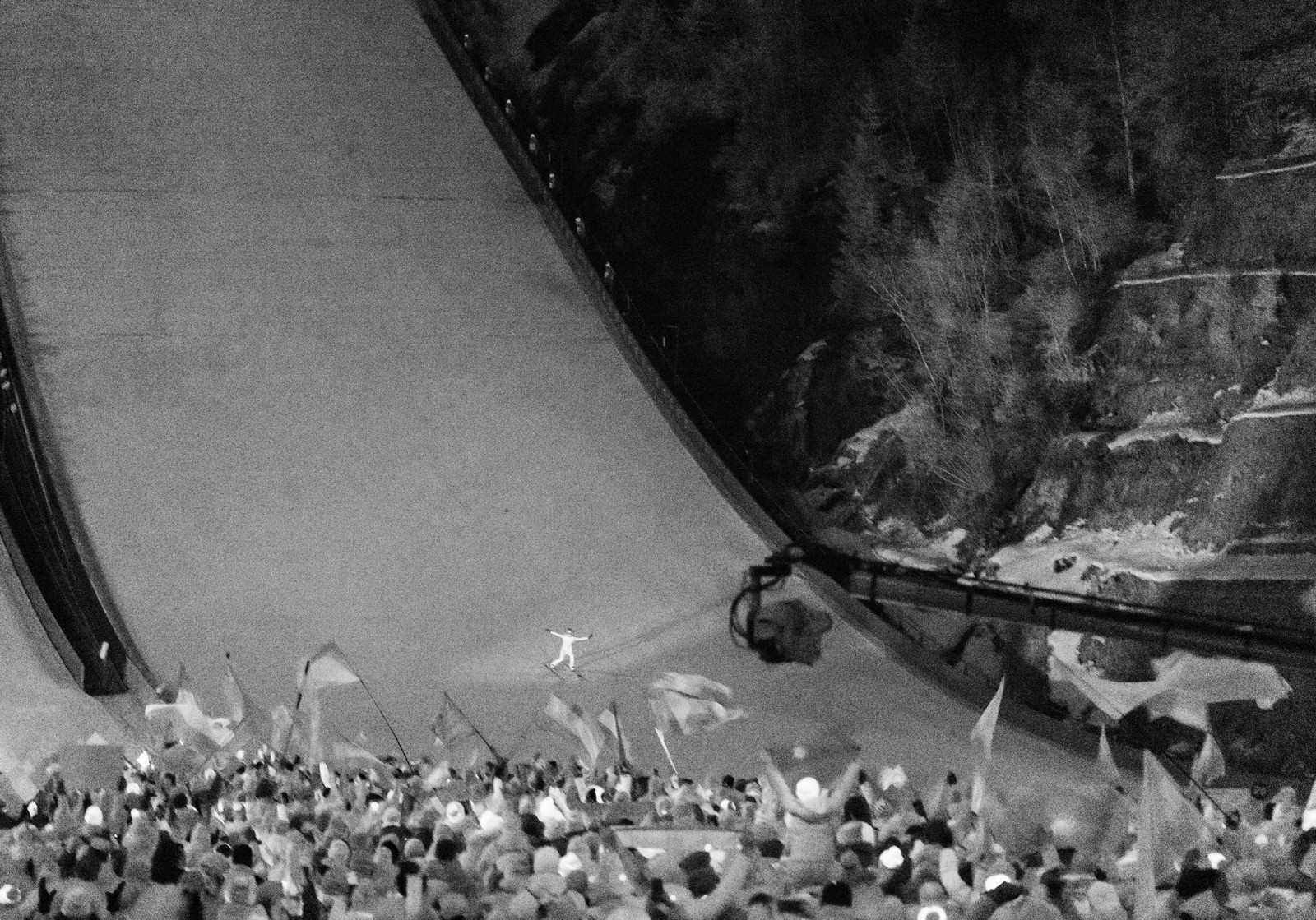 An infrared image of a ski jumper at the bottom of a steep hill, cheered by a crowd.