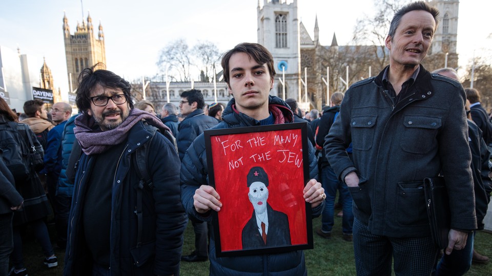 A protester holds a framed image of Labour leader Jeremy Corbyn and the words "For The Many Not The Jew."