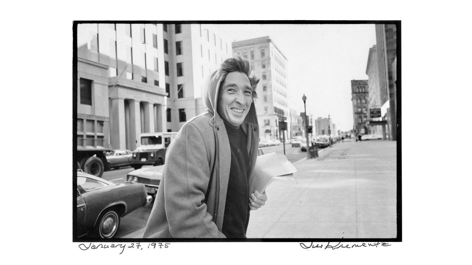 A man in a hoodie on a street with many papers in his hand.