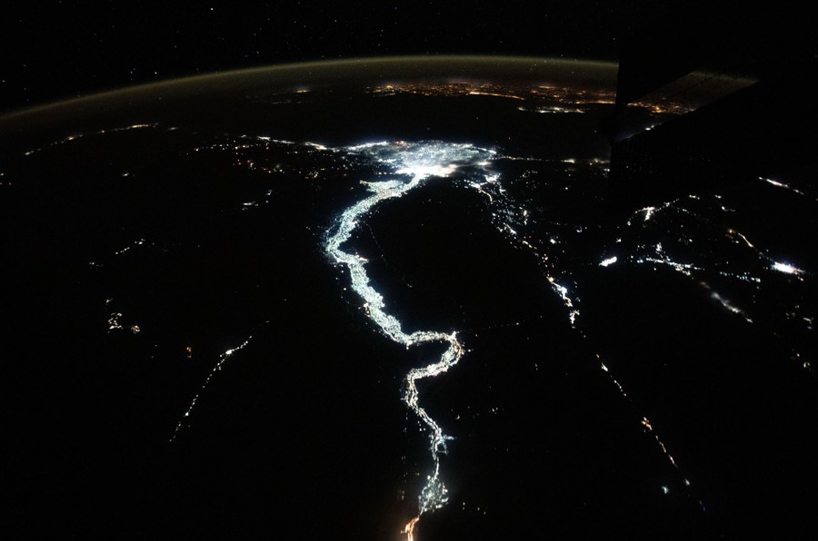 A twisting line of lights marks the path of a long river in a desert area, seen from orbit at night.