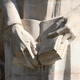 A close-up image of a statue, showing a pair of hands holding a book