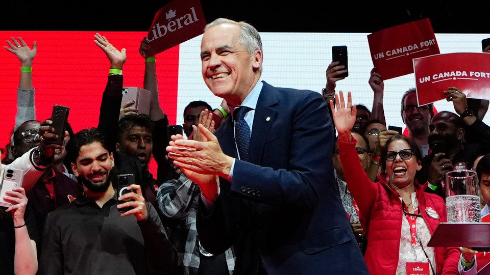 Mark Carney smiles and claps in front of a group of supporters waving, recording with their phones, and holding signs