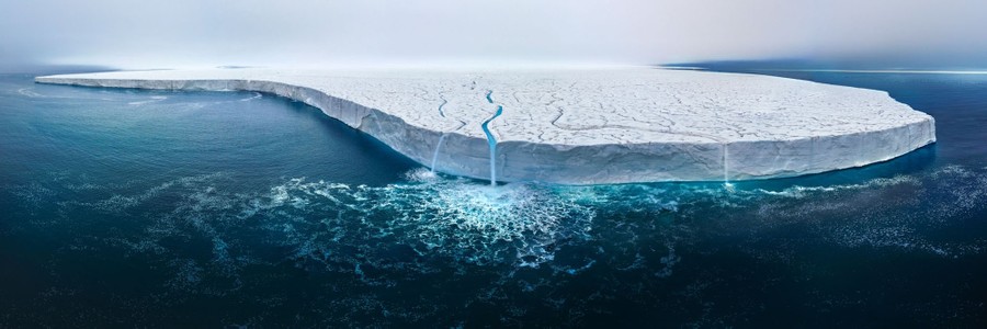 A wide view of several waterfalls cascading into the sea from a broad sheet of ice