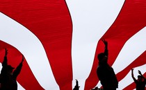 Silhouettes of people hold up a giant flag with red and white stripes