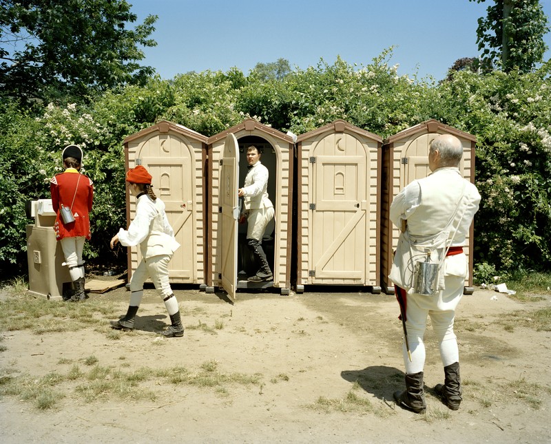 photo of several reenactors dressed as British soldiers waiting for and exiting a row of modern portable toilets