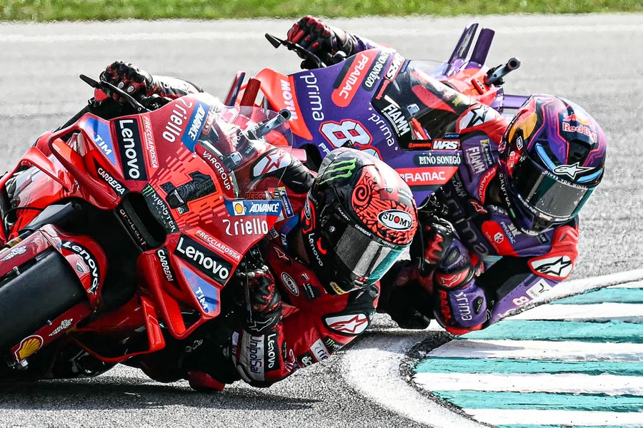 Two motorcycle riders lean close to the ground in a turn during a race.