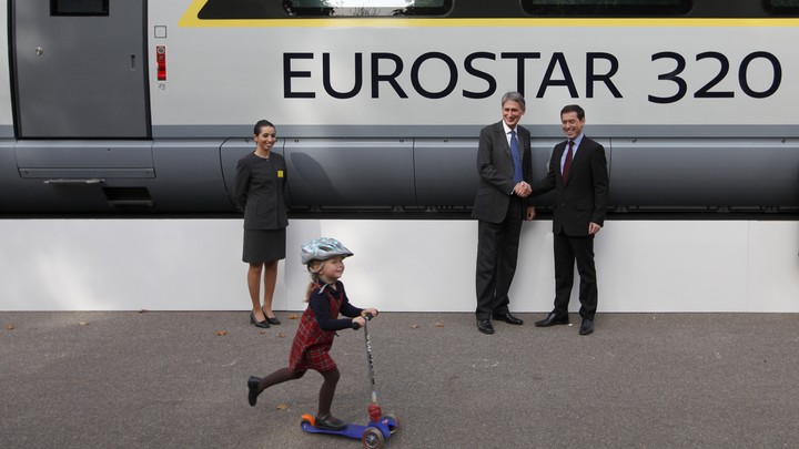 A girl rides a scooter past a commuter train