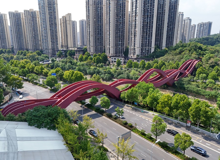 An aerial view of an intertwined set of undulating pedestrian bridges over a highway beside many tall buildings