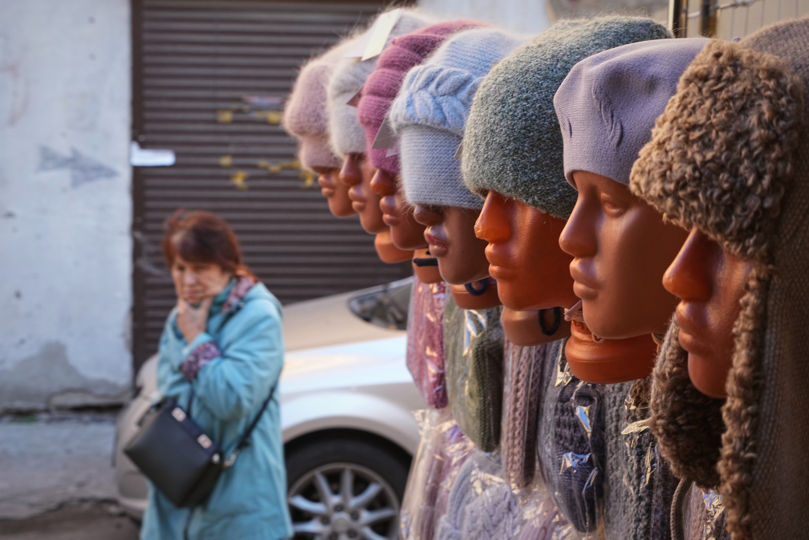 A person walks past a storefront with a half-dozen mannequin heads displaying warm hats.