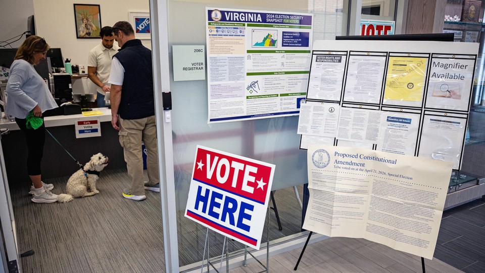 Photograph of an office with a red, white, and blue “VOTE HERE” sign with signs about election security, voting instructions, and a proposed constitutional amendment behind it