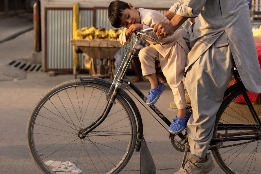 A boy sleeps as he leans on a bicycle's handlebars.